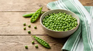 Ciotola di piselli freschi su tavolo in legno con tovagliolo verde a righe