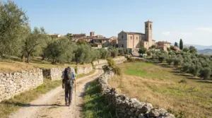 Persona che cammina lungo un sentiero di campagna verso un borgo antico sul Cammino di San Francesco